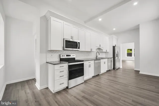 a kitchen with stainless steel appliances granite countertop a stove top oven a sink and white cabinets with wooden floor