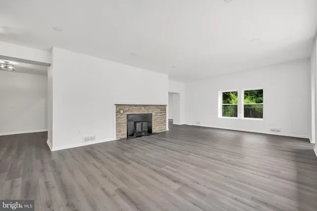 an empty room with wooden floor fireplace and windows