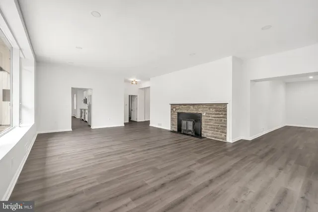 a view of an empty room with wooden floor fireplace and a window