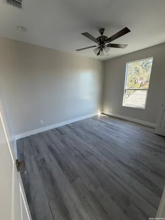 an empty room with wooden floor fan and windows