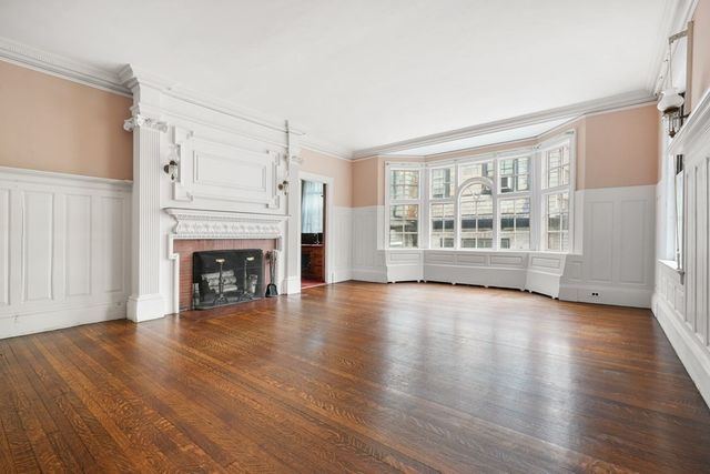 an empty room with wooden floor fireplace and windows