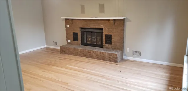 a view of an empty room with wooden floor and fireplace