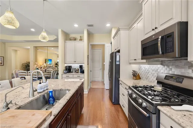 a kitchen with stainless steel appliances granite countertop a stove top oven a sink dishwasher a dining table and chairs with wooden floor