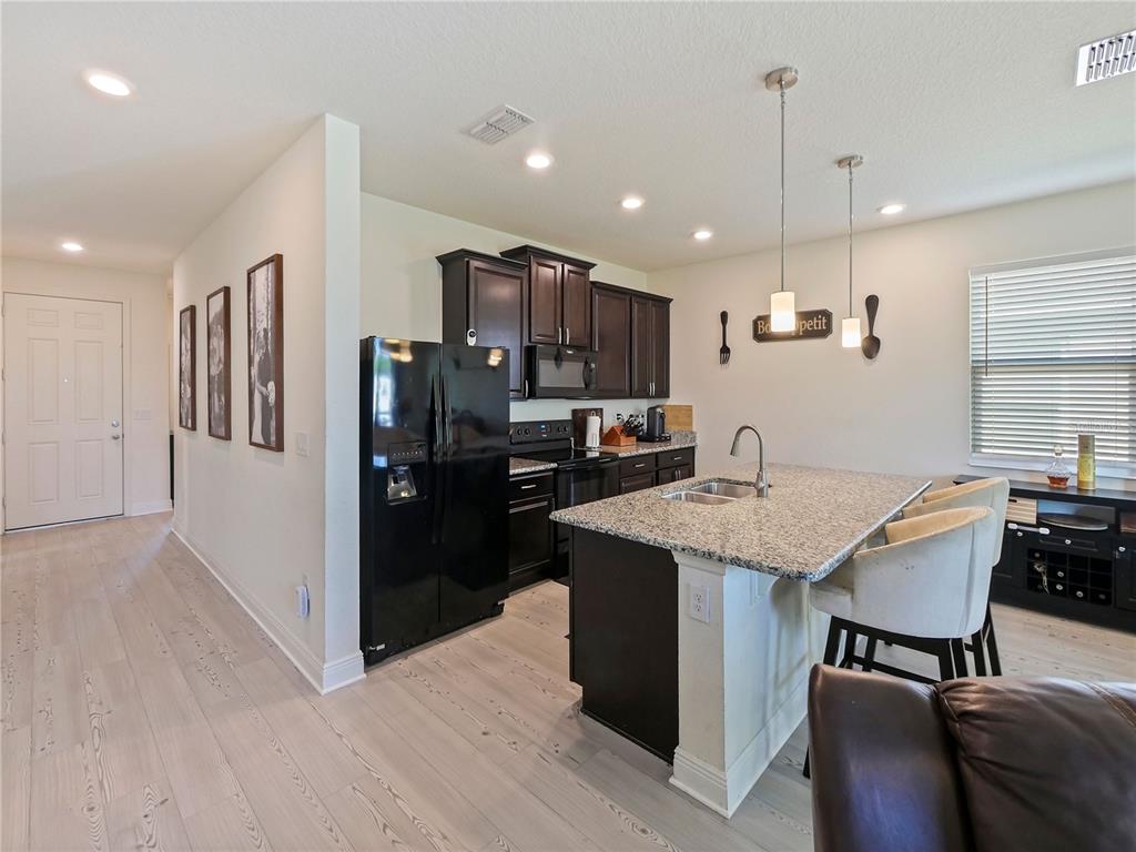 4553 Baler Trails Drive St. Cloud, FL 34772 - Photo 10 of 32 a kitchen with stainless steel appliances kitchen island granite countertop a refrigerator a stove a sink a dining table and chairs with wooden floor
