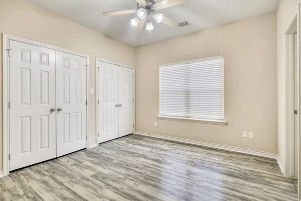an empty room with wooden floor chandelier fan and windows