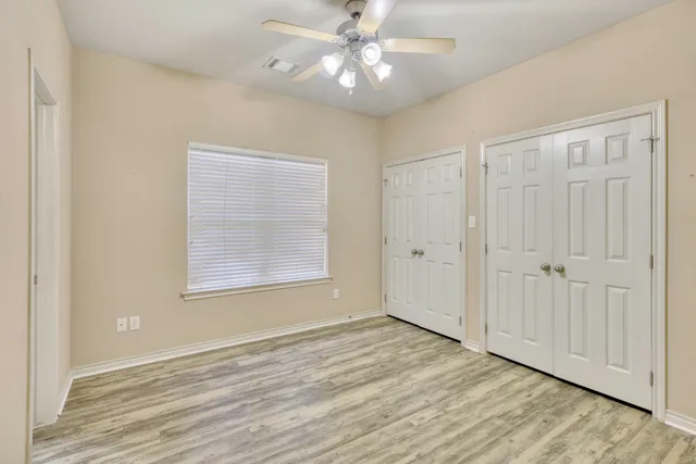 an empty room with wooden floor chandelier fan and windows