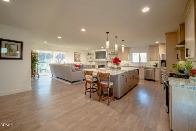 a living room with stainless steel appliances kitchen island granite countertop a table chairs and a refrigerator