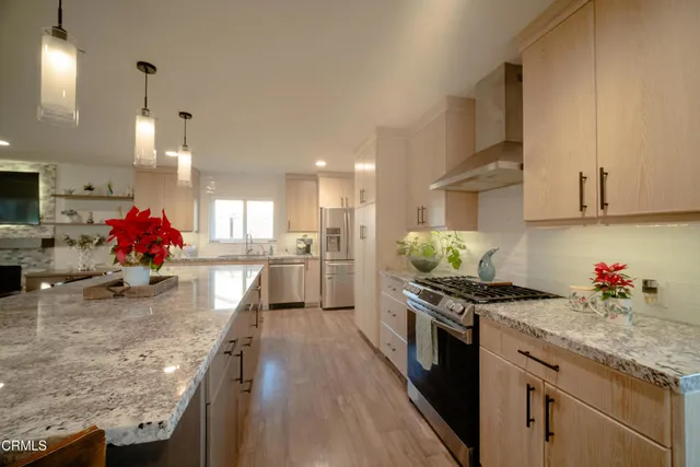 a kitchen with granite countertop a stove a sink a refrigerator and white cabinets with wooden floor