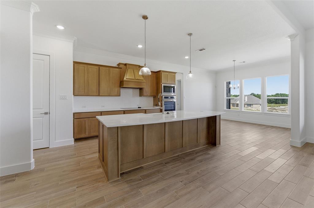 815 Vly Rdg Road Van Alstyne, TX 75495 - Photo 12 of 29 Open-concept kitchen featuring an oversized island with pendant lighting, wood-finish cabinetry, built-in double ovens, and tile flooring