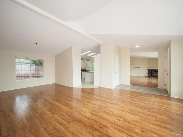 a view of empty room with wooden floor and kitchen view