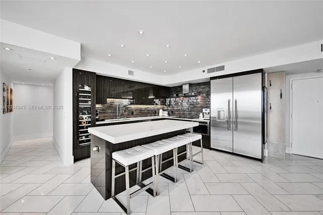 a kitchen with stainless steel appliances kitchen island granite countertop a table chairs and a refrigerator