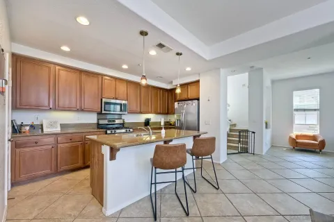 a kitchen with stainless steel appliances granite countertop a stove top oven a refrigerator a sink a dining table and chairs with wooden floor