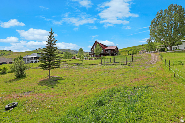 306 Spring Road Preston, ID 83263 - Photo 43 of 55 Expansive sloping green landscape with a dirt path leading towards a red-roofed residence featuring a raised deck