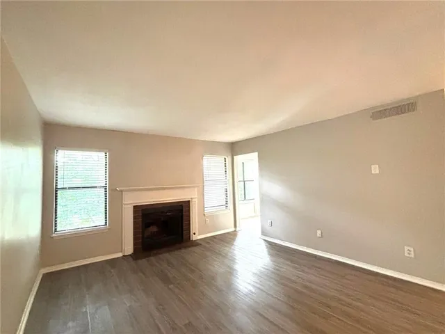 an empty room with wooden floor fireplace and windows