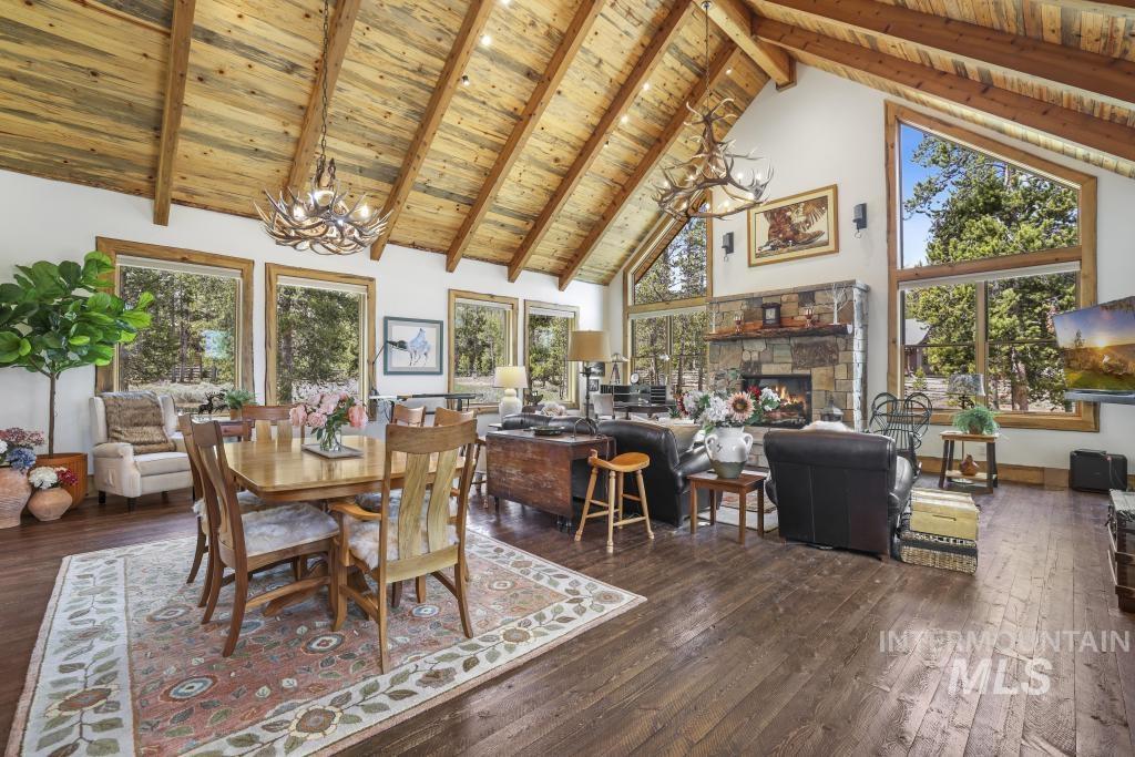 65 Goat Creek Way Stanley, ID 83278 - Photo 10 of 32 Spacious living area featuring a vaulted wood-paneled ceiling, exposed wood beams, a stone fireplace, large picture windows, and wood-finish flooring