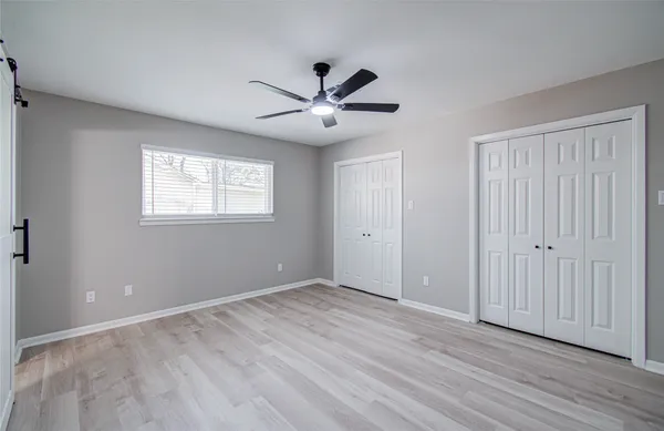 an empty room with wooden floor ceiling fan and windows