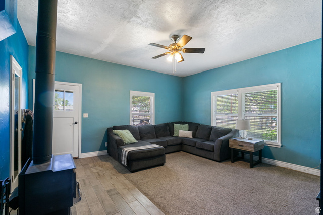 137 West 200 S Street Fairview, UT 84629 - Photo 11 of 34 Spacious living area featuring a wood-burning stove, ceiling fan, and two large windows with blinds
