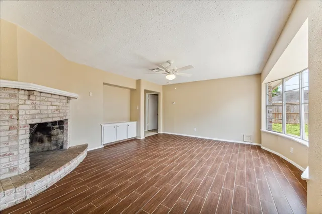 an empty room with wooden floor fireplace and windows