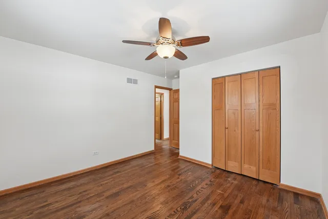 a view of an empty room with wooden floor and a ceiling fan
