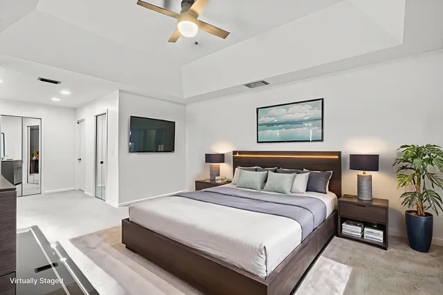 a bedroom with a large bed a flat tv screen and potted plant on the dresser