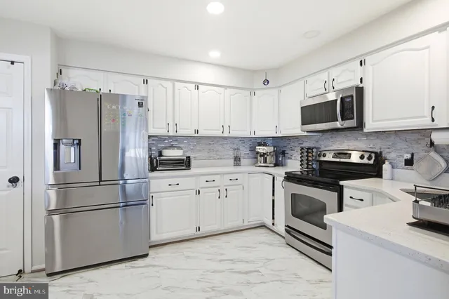 a kitchen with stainless steel appliances granite countertop a refrigerator stove a sink and white cabinets