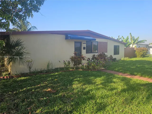 a view of a yard in front of a house with plants and palm trees