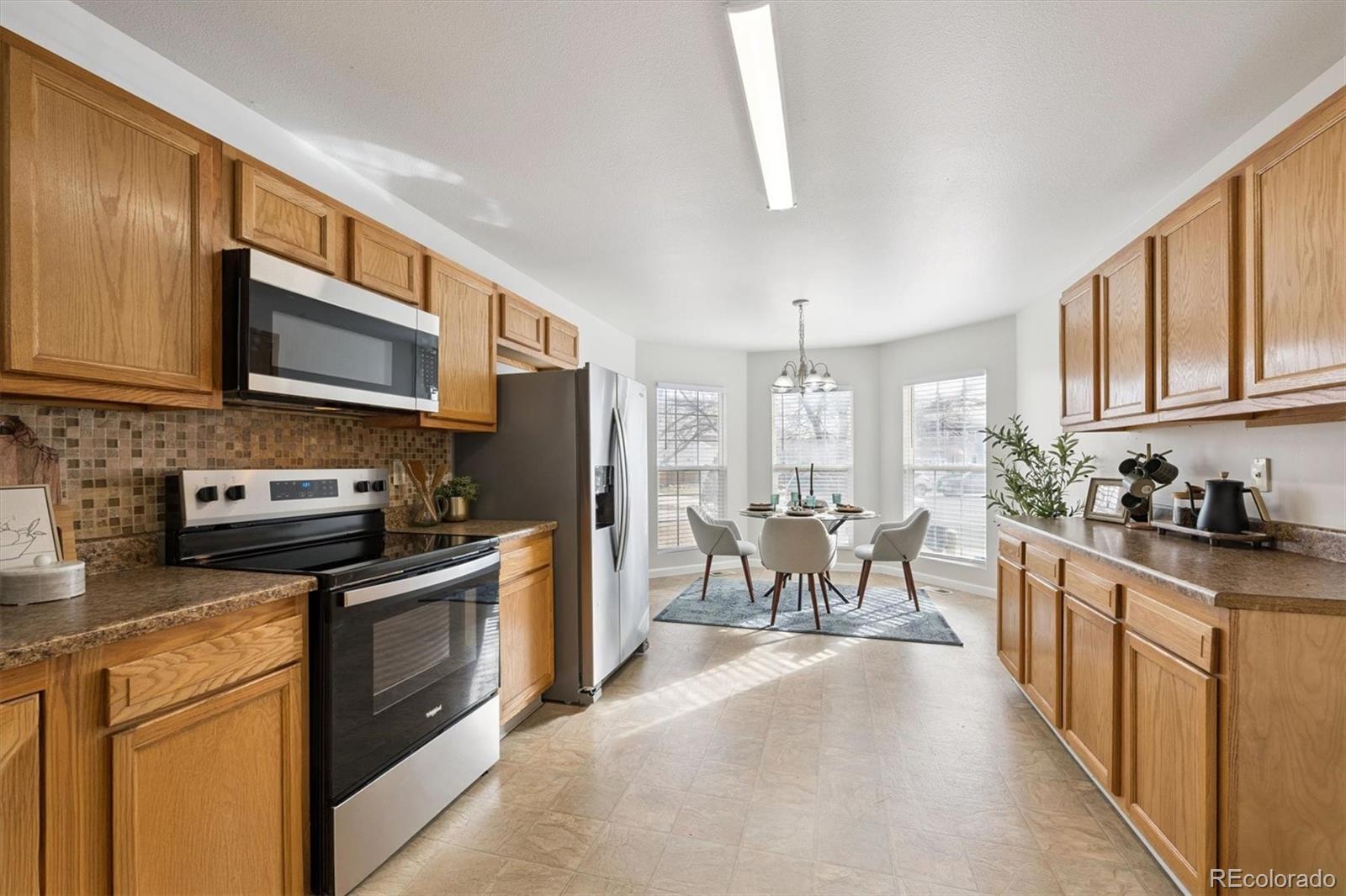 5241 Helena Street Denver, CO 80239 - Photo 9 of 28 a kitchen with stainless steel appliances granite countertop a stove top oven a sink dishwasher a dining table and chairs with wooden cabinets