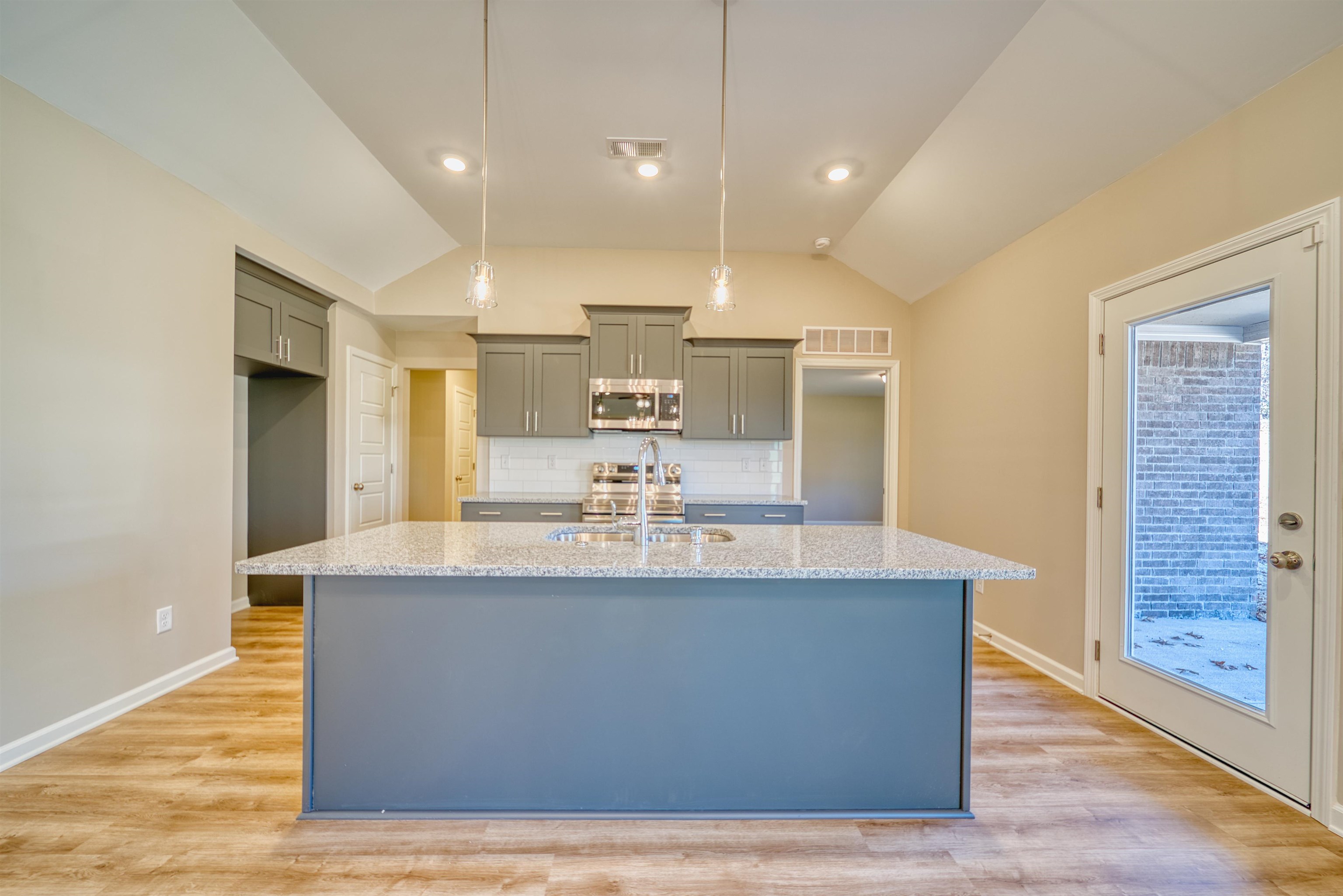102 Stone Brook Cove Ripley, TN 38063 - Photo 23 of 32 Kitchen featuring gray cabinets, lofted ceiling, an island with sink, light stone counters, and decorative light fixtures