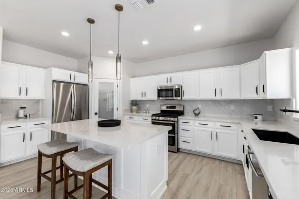 a kitchen with stainless steel appliances a stove a sink a stove a refrigerator and white cabinets with wooden floor