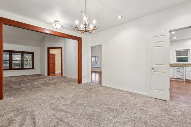 a view of an empty room with chandelier and kitchen