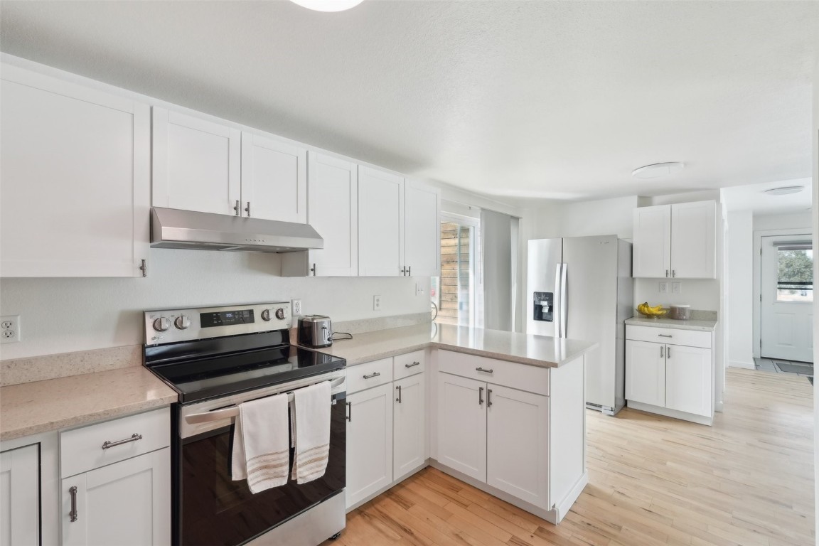 416 Cascade Circle Silverthorne, CO 80498 - Photo 2 of 49 Kitchen with light wood finished floors, a peninsula, white cabinets, under cabinet range hood, and appliances with stainless steel finishes