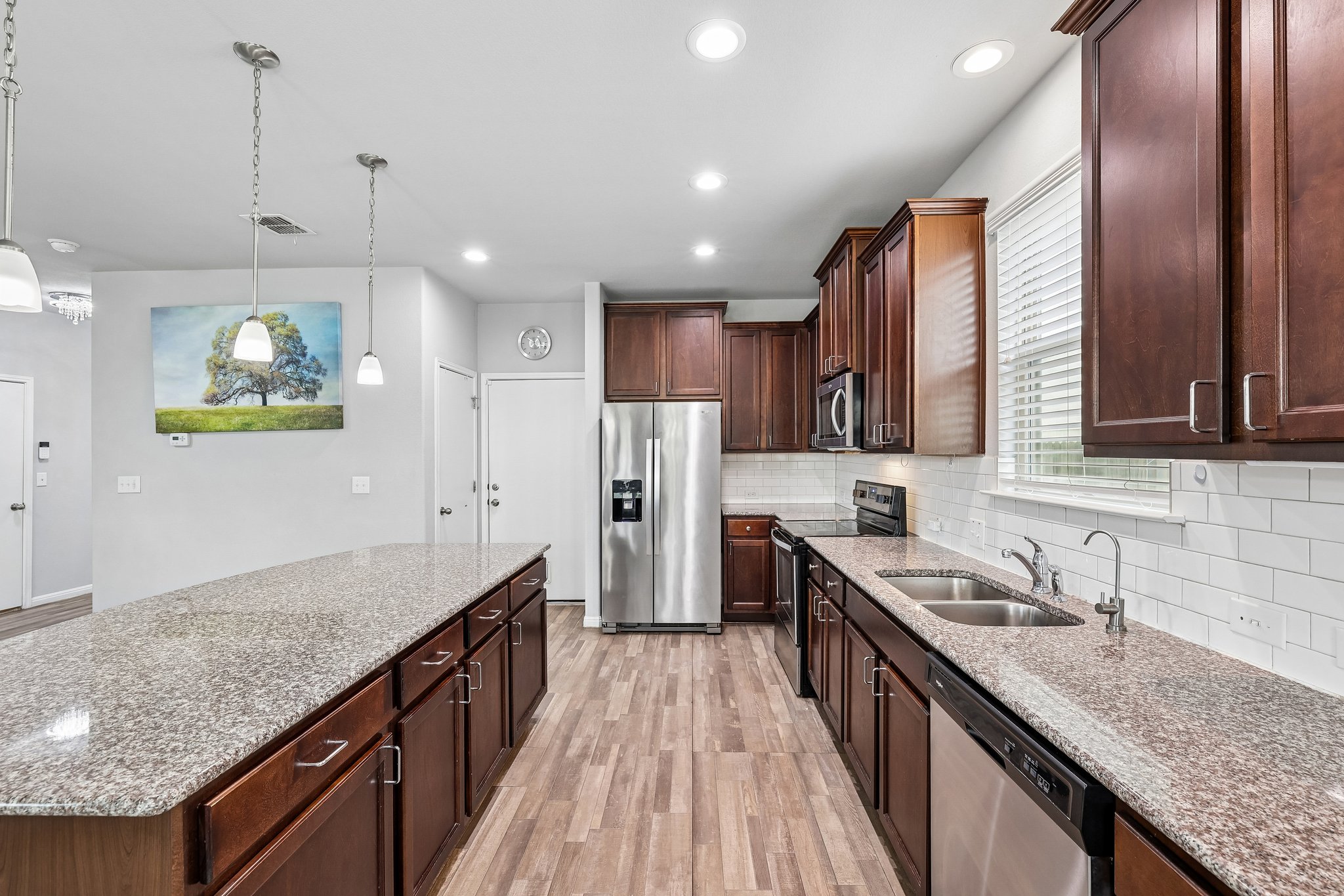 387 Guemal Road Buda, TX 78610 - Photo 12 of 39 Kitchen featuring an extended island with a stone-finish countertop, wood-finish flooring, dark wood cabinetry, stainless steel appliances, and recessed lighting