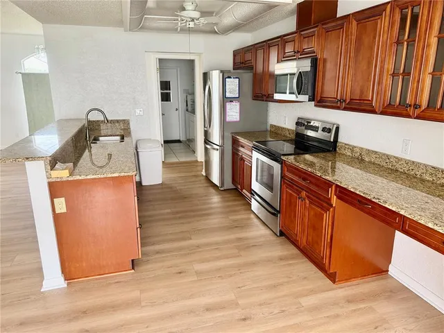 a kitchen with stainless steel appliances granite countertop a stove top oven a refrigerator a sink dishwasher with wooden cabinets and floor