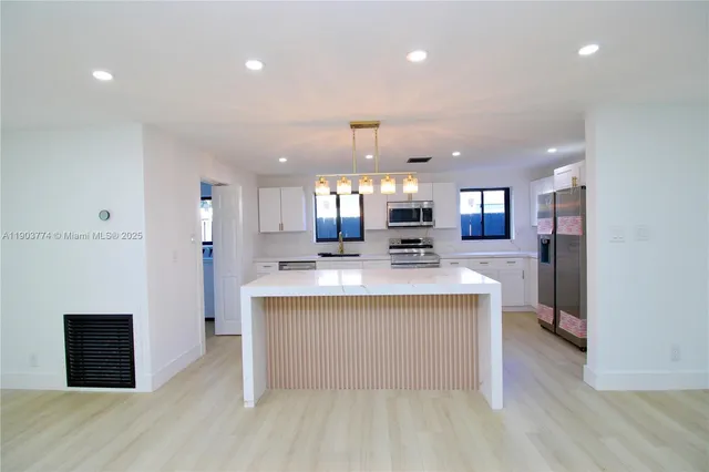 a large white kitchen with kitchen island a sink dishwasher a stove and a refrigerator with wooden floor