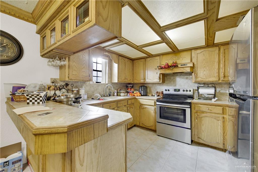 309 Domingo Navarez Street Rio Grande City, TX 78582 - Photo 6 of 14 Kitchen featuring a peninsula, stainless steel appliances, tile countertops, glass fronted cabinets, and light tile patterned floors