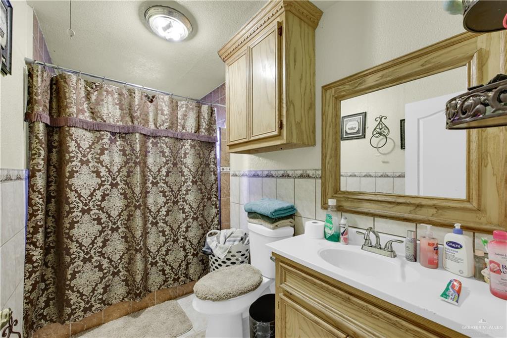 309 Domingo Navarez Street Rio Grande City, TX 78582 - Photo 9 of 14 Bathroom featuring a shower with shower curtain, vanity, tile walls, wainscoting, and a textured ceiling