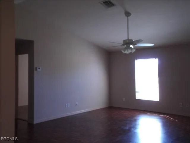 an empty room with wooden floor chandelier fan and windows