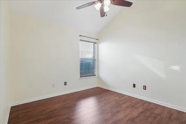 an empty room with a chandelier fan and wooden floor