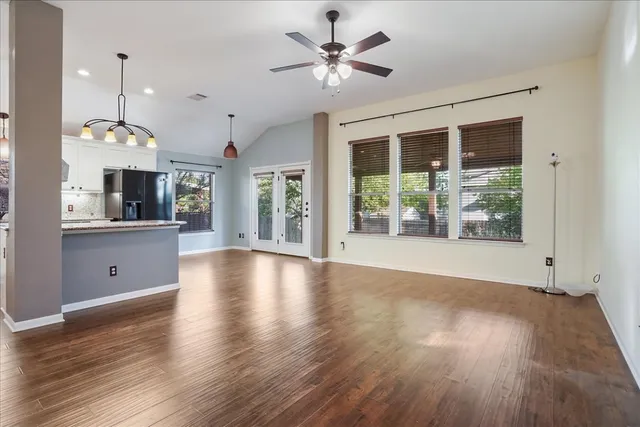 a view of an empty room with window wooden floor and a kitchen view