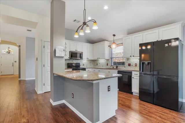 a kitchen with stainless steel appliances granite countertop a refrigerator a sink dishwasher a stove and white cabinets with wooden floor