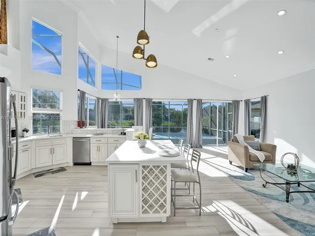 a kitchen with stainless steel appliances kitchen island granite countertop a dining table chairs and a refrigerator