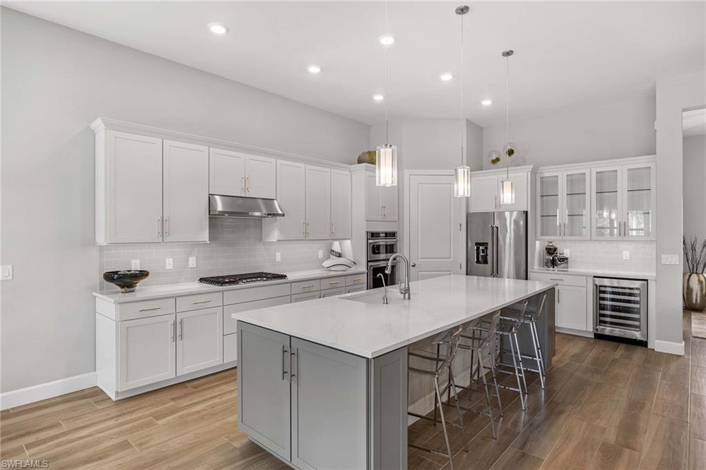 9309 Surfbird Court Naples, FL 34120 - Photo 11 of 45 Kitchen with white cabinets, a kitchen bar, stainless steel appliances, wine cooler, and glass insert cabinets