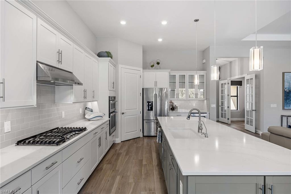9309 Surfbird Court Naples, FL 34120 - Photo 12 of 45 Kitchen featuring a kitchen island with sink, decorative light fixtures, white cabinetry, appliances with stainless steel finishes, and dark wood finished floors