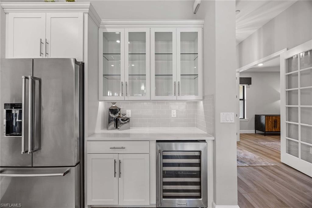 9309 Surfbird Court Naples, FL 34120 - Photo 13 of 45 Bar area with high quality fridge, white cabinets, beverage cooler, light stone counters, and glass insert cabinets