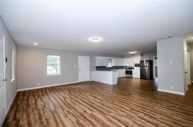 a view of empty room with wooden floor and kitchen