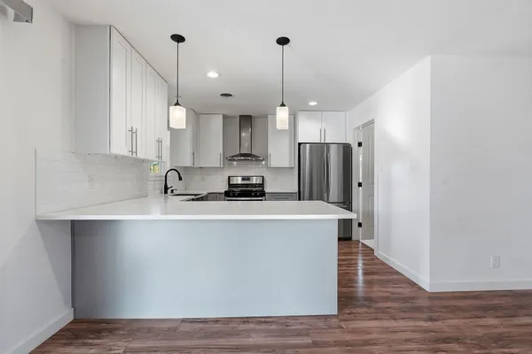 a kitchen with stainless steel appliances a refrigerator a sink dishwasher a stove and white cabinets with wooden floor