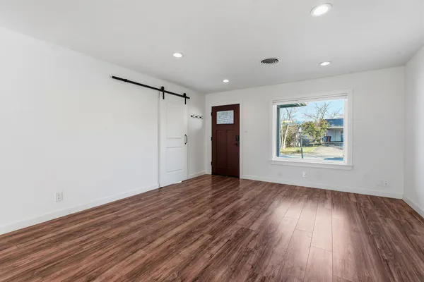 a view of an empty room with wooden floor and a window