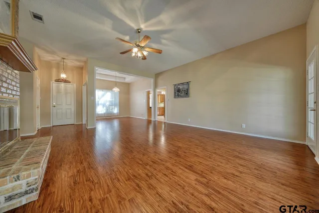 a view of an empty room with wooden floor and a ceiling fan