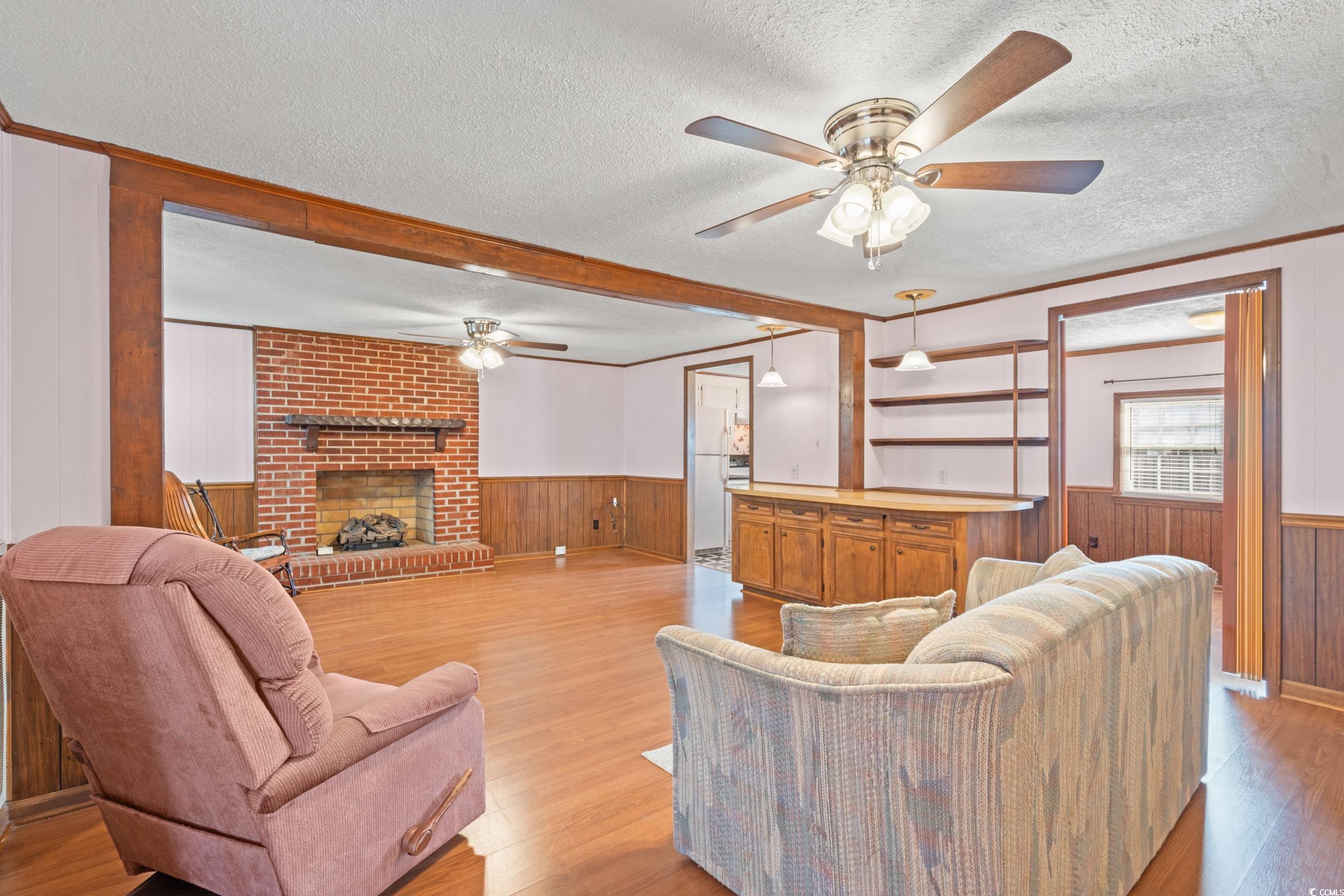 4422 Grady Road Mullins, SC 29574 - Photo 6 of 28 Living area with a textured ceiling, wooden walls, light wood-style floors, ornamental molding, and a ceiling fan