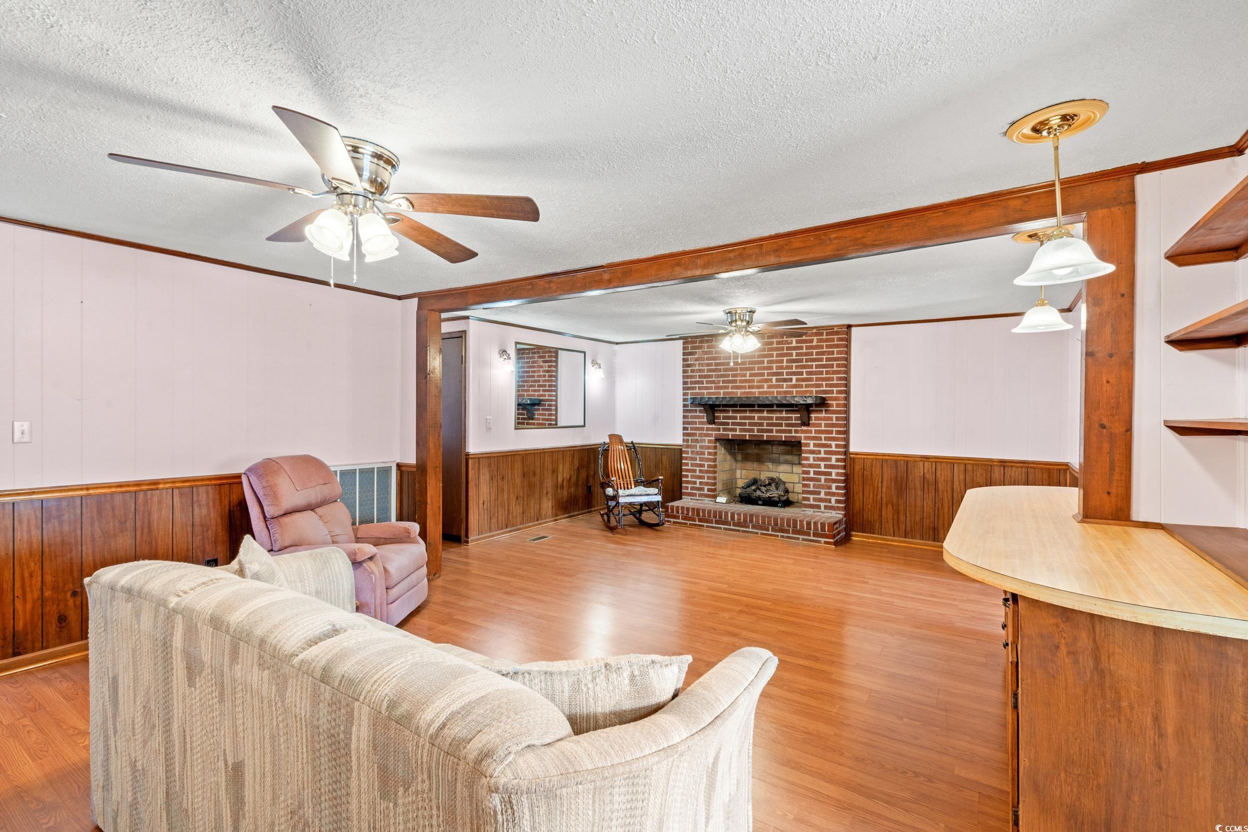 4422 Grady Road Mullins, SC 29574 - Photo 7 of 28 Living room featuring wooden walls, ceiling fan, light wood-type flooring, crown molding, and a textured ceiling